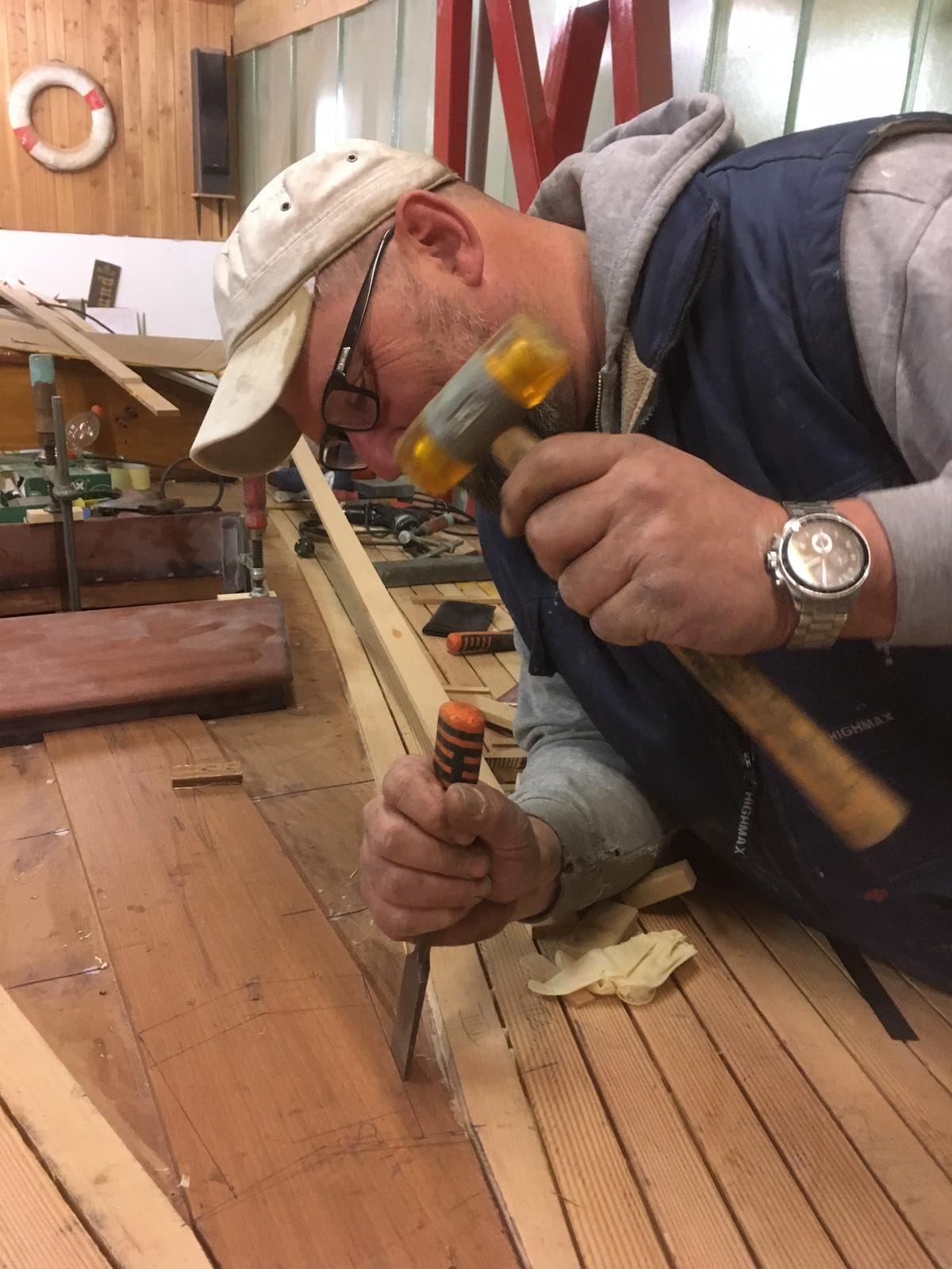 Ein Bootsbauer arbeitet mit dem Stecheisen am neuen Deck aus Oregon-Pine.