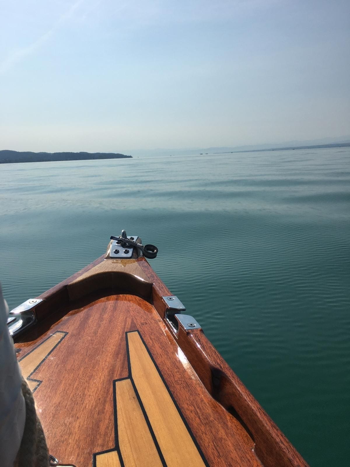 Blick über den Bug auf den spiegelglatten See im Morgendunst.