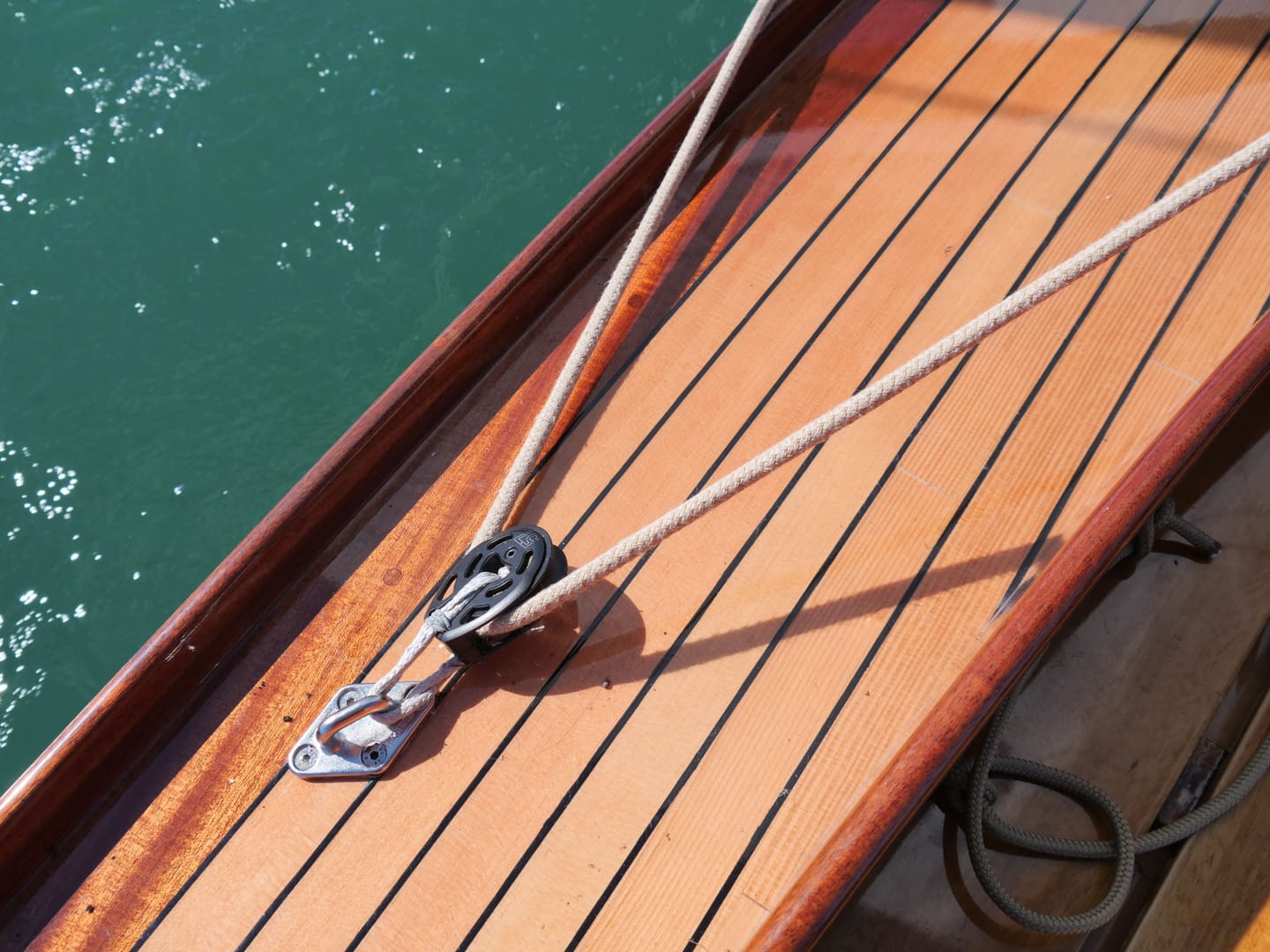 Schot mit Umlenkblock auf dem lackierten Deck, daneben das Wasser.