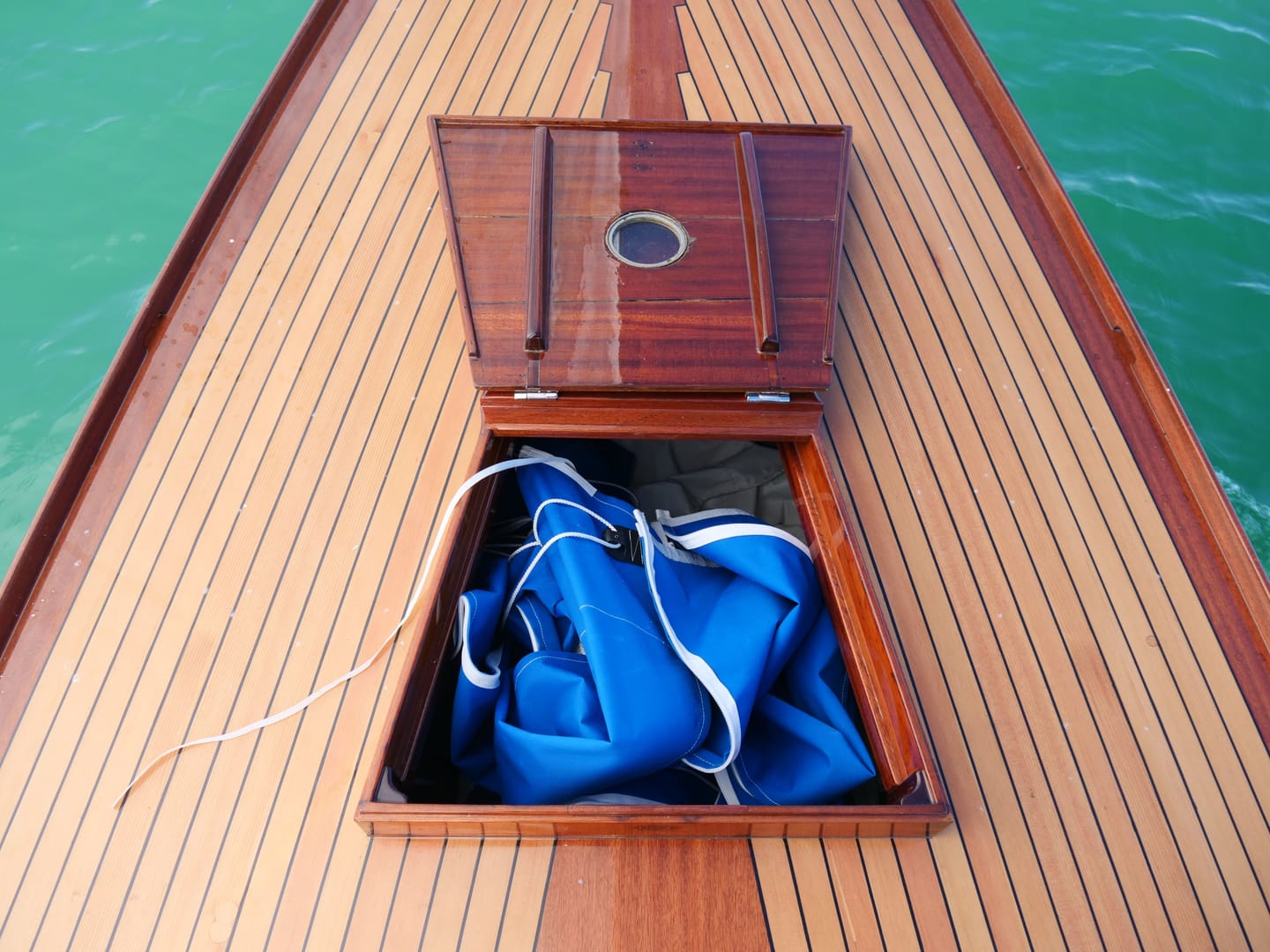 Geöffnete Vorschiffsluke aus Mahagoni mit dem blauen Segelsack darin.